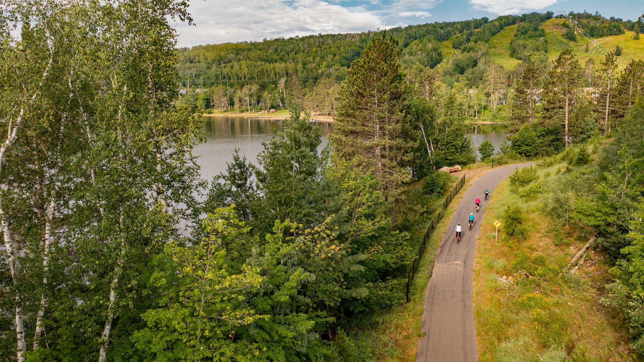 Cyclists riding a paved trail beside a lake on the East Range